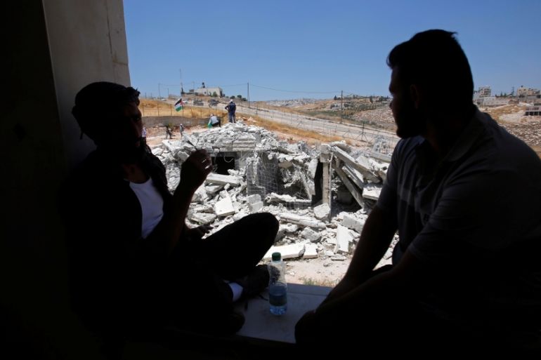 Men sit by a building window as a Palestinian house demolished by Israeli forces is seen in the village of Sur Baher which sits on either side of Israeli barrier in East Jerusalem and the Israeli-