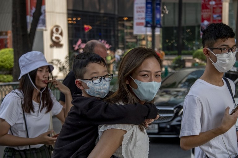 Chinese family wearing face masks walk in a pedestrian crossing in Bangkok, Thailand, Wednesday, Jan. 29, 2020. Tourism Council of Thailand said Tuesday that new coronavirus outbreak estimated to cost