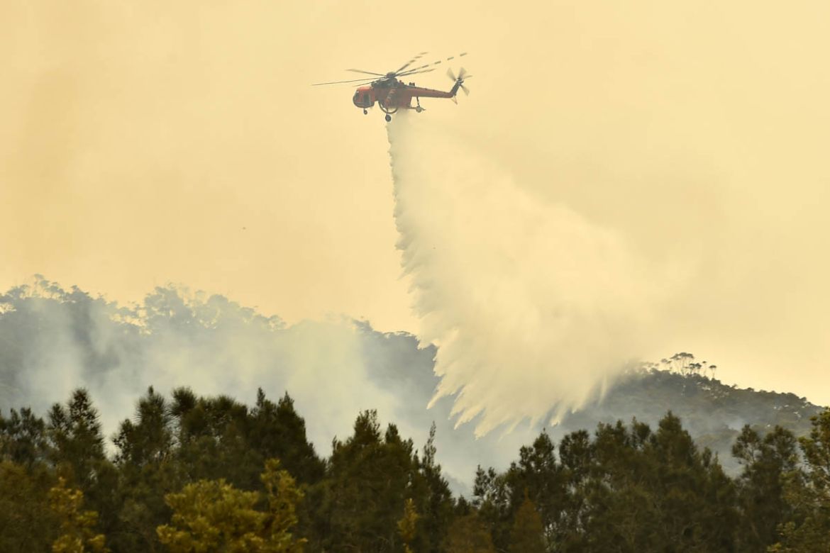 A helicopter drops water on a bushfire outside of Batemans Bay in New South Wales on January 2, 2020. - Australia authorised the forced evacuation of residents on January 2 amid a mass exodus of touri