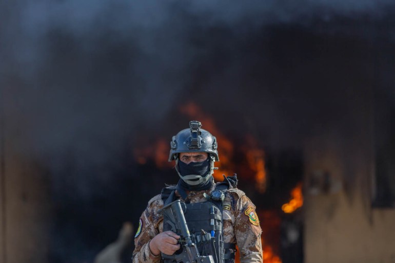 An Iraqi soldier stands guard in front of smoke rising from a fire set by pro-Iranian militiamen and their supporters in the U.S. embassy compound, Baghdad, Iraq, Wednesday, Jan. 1, 2020. U.S. troops
