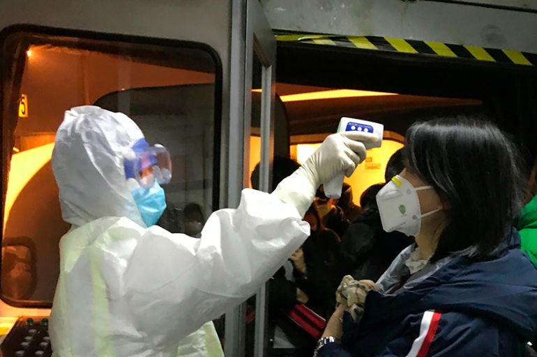 Health Officials in hazmat suits check body temperatures of passengers arriving from the city of Wuhan Wednesday, Jan. 22, 2020, at the airport in Beijing, China. Nearly two decades after the disastro