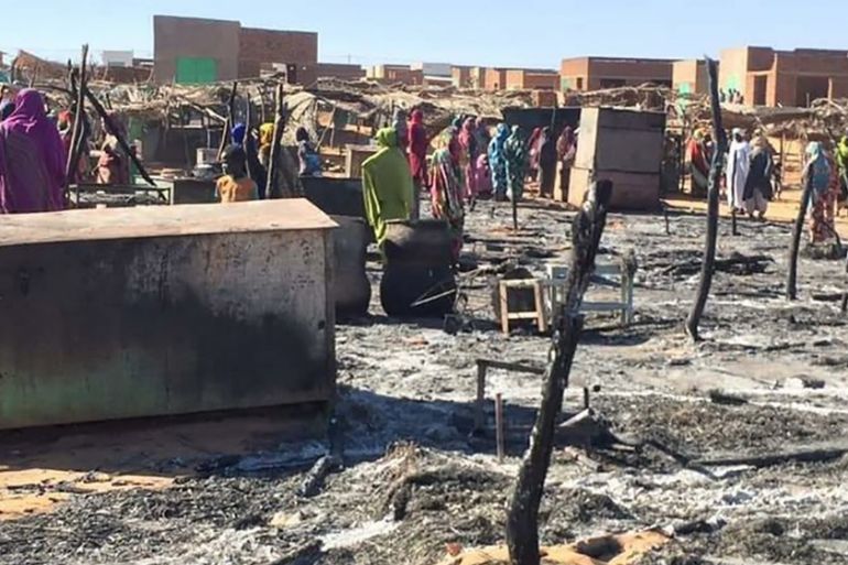 In this Sunday, Dec. 29, 2019 photo, residents of a refugee camp gather around the burned remains of makeshift structures, in Genena, Sudan. A Sudanese aid group says sporadic tribal clashes between A