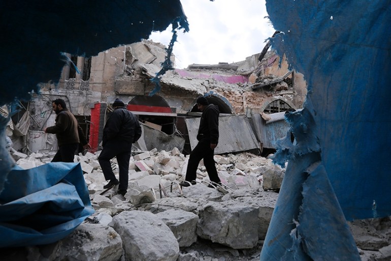 People walk past destruction by the government airstrikes in the town of Ariha, in Idlib province, Syria, Wednesday, Jan. 15, 2020. Syrian government warplanes struck a market and an industrial area W