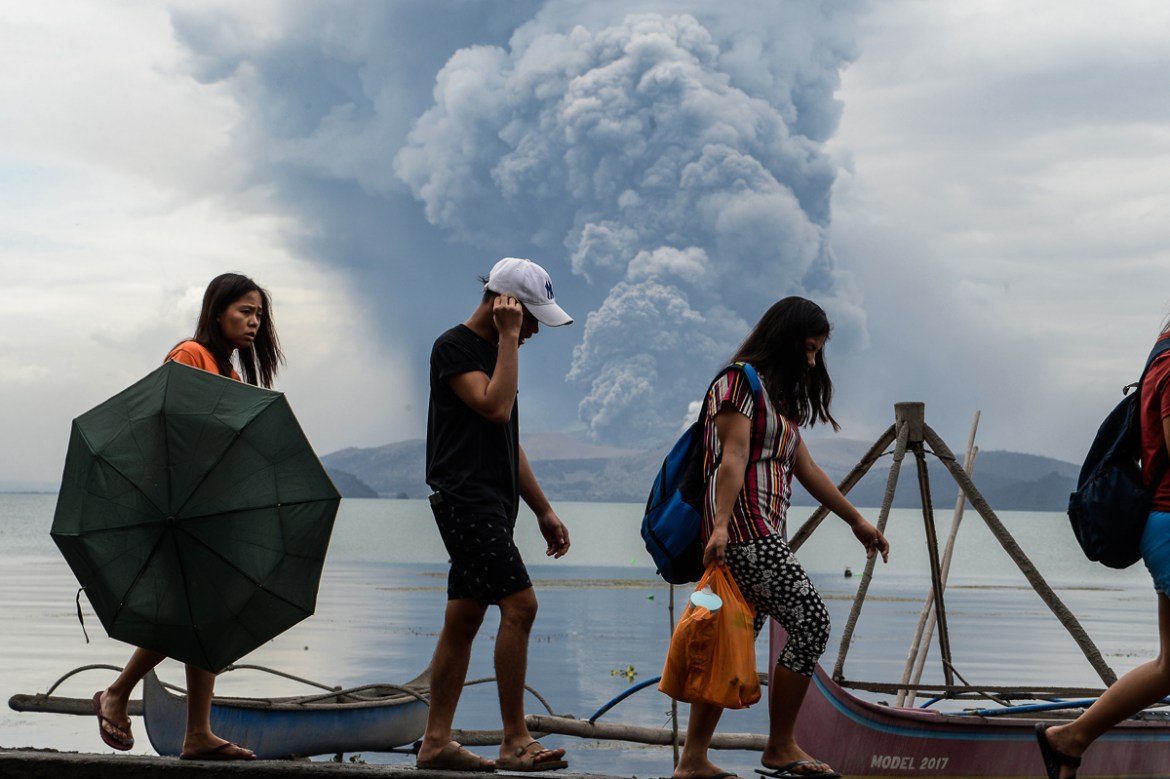 Residents walk past wooden boats as Taal volcano erupts, in Tanauan town, Batangas province south of Manila on January 13, 2020. - Lava and broad columns of ash illuminated by lightning spewed from a