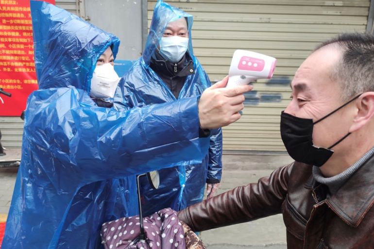 Worker takes body temperature measurement of a man at the entrance to a residential compound following an outbreak of the new coronavirus in Wuhan