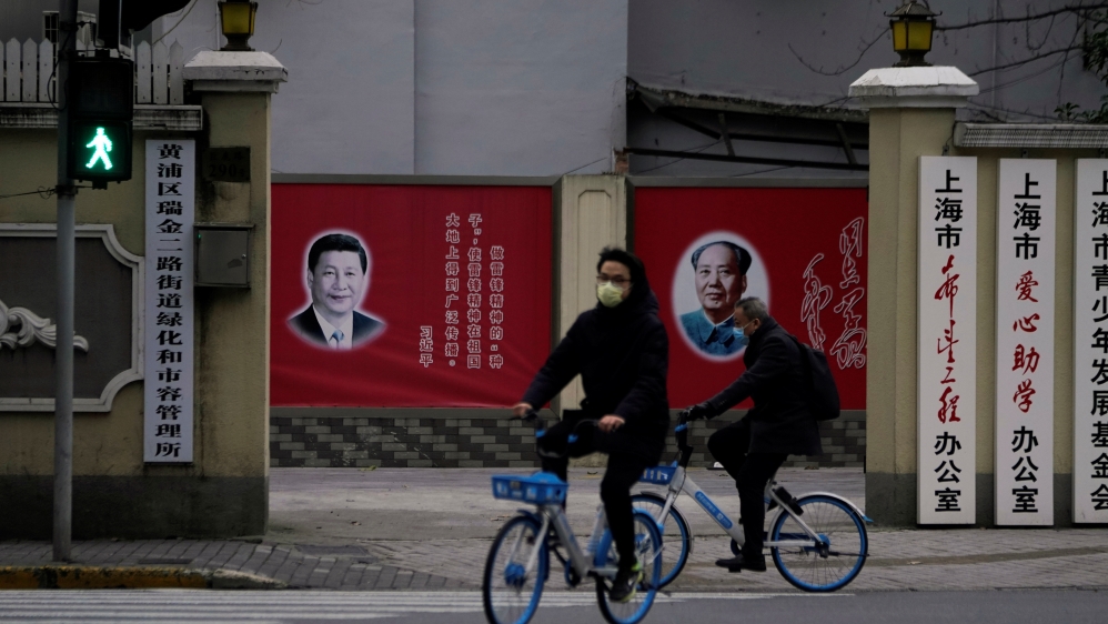 People wearing masks pass by portraits of Chinese President Xi Jinping and late Chinese chairman Mao Zedong as the country is hit by an outbreak of the novel coronavirus, on a street in Shanghai