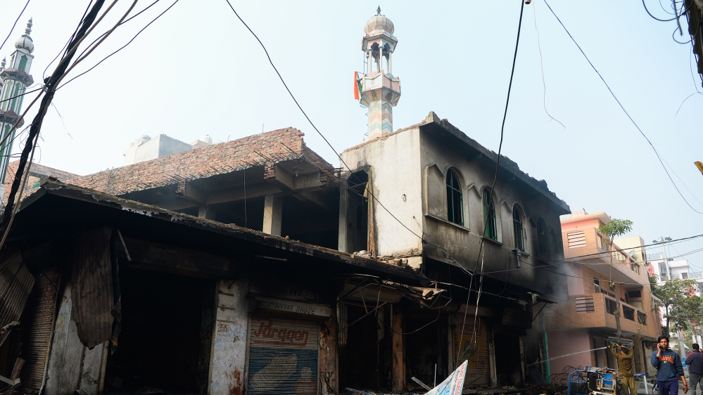 A man (R) speaks on his mobile phone as he walks past a burnt-out mosque and shops following clashes between people supporting and opposing a contentious amendment to India's citizenship law, in New D