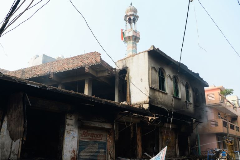 A man (R) speaks on his mobile phone as he walks past a burnt-out mosque and shops following clashes between people supporting and opposing a contentious amendment to India''s citizenship law, in New D