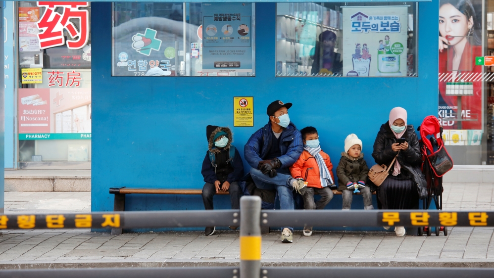 Tourists wearing masks as a preventive measure against the coronavirus sit at a Myeongdong station bus stop in Seoul