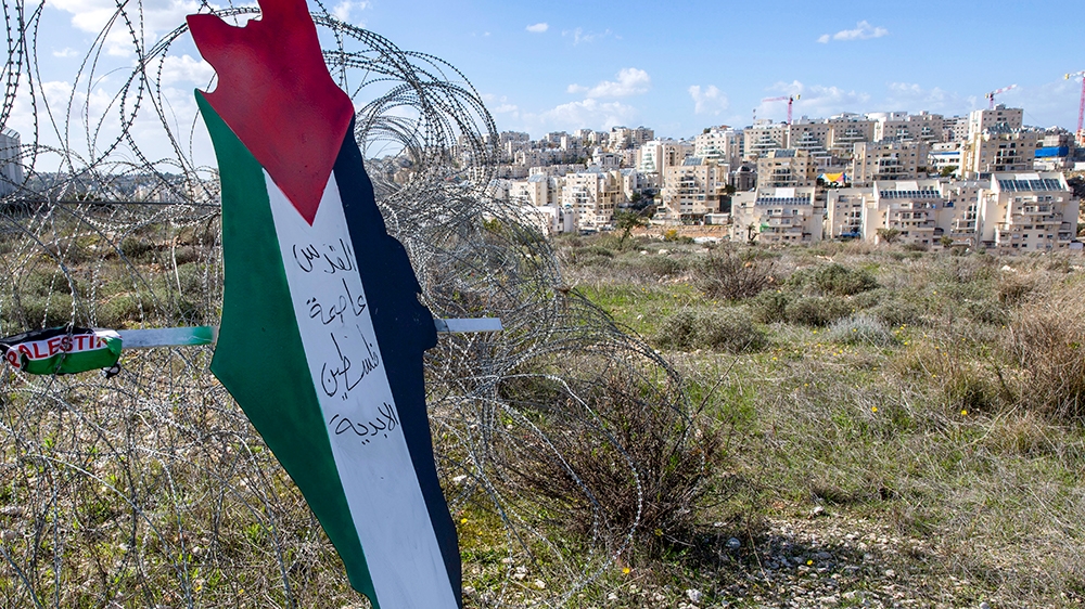 Protesters post a placard with the colors of the Palestinian flags and Arabic that reads “Jerusalem is the eternal capital of Palestine,” at a barbed wire surrounding the Israeli separation wall and t