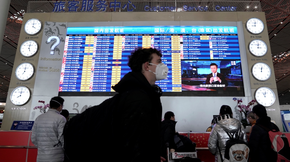 A foreign traveller wearing a mask walks past a departures information board at Beijing International Airport in Beijing