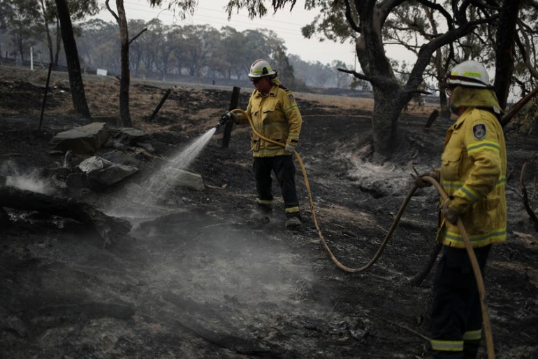 Firefighters spray water on smouldering patches left in the wake of a bushfire near Bumbalong