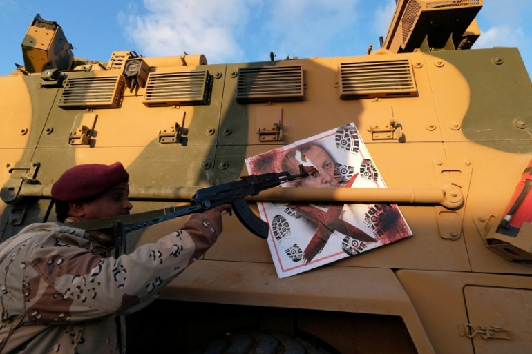 A member of Libyan National Army (LNA) commanded by Khalifa Haftar, points his gun to the image of Turkish President Tayyip Erdogan hanged on a Turkish military armored vehicle, which LNA said they co