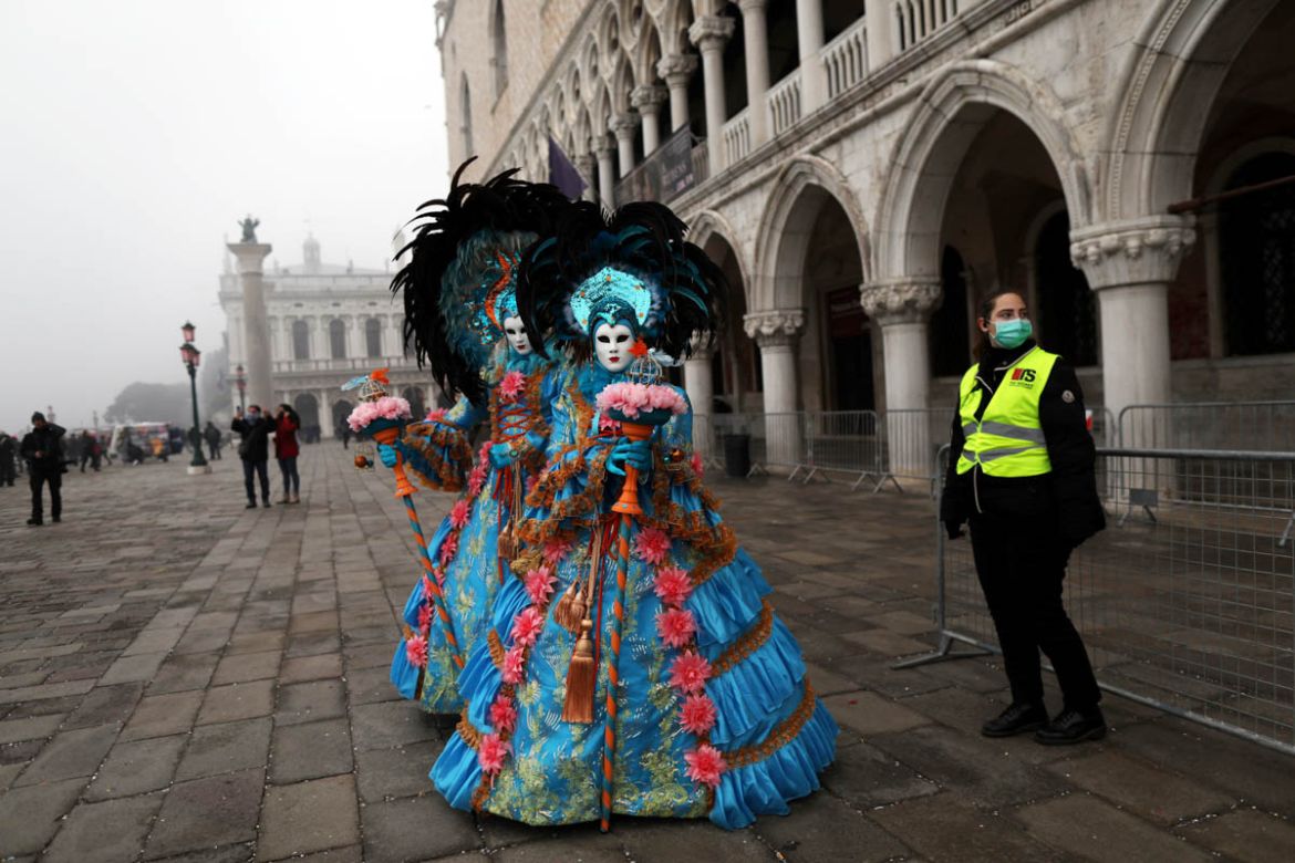 A policewoman wearing a protective mask stands next to carnival revellers at Venice Carnival, which the last two days of, as well as Sunday night''s festivities, have been cancelled because of an outbr