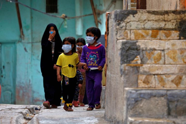 Iraqi children wear protective masks as they walk near a religious school where the first coronavirus case was detected, following the outbreak of the new coronavirus, in the holy city of Najaf, Iraq