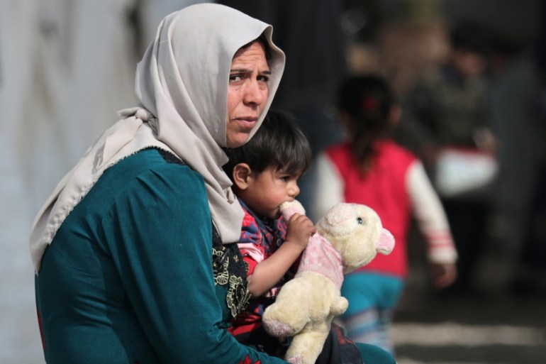 An internally displaced child carries a stuffed animal as he sits on a woman''s lap at a makeshift camp in Afrin