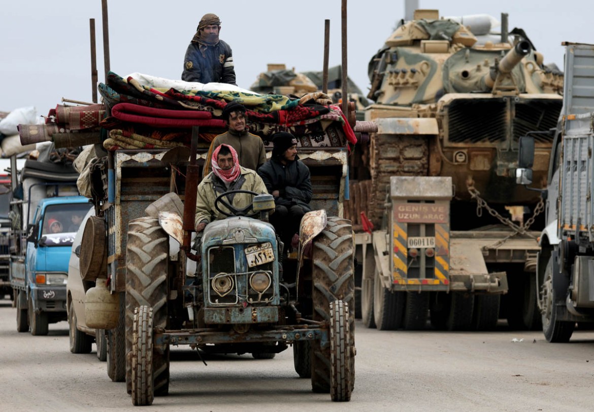 Internally displaced Syrians from western Aleppo countryside, ride on a tractor with belongings past Turkish military vehicles in Hazano near Idlib, Syria, February 11, 2020. REUTERS/Khalil Ashawi