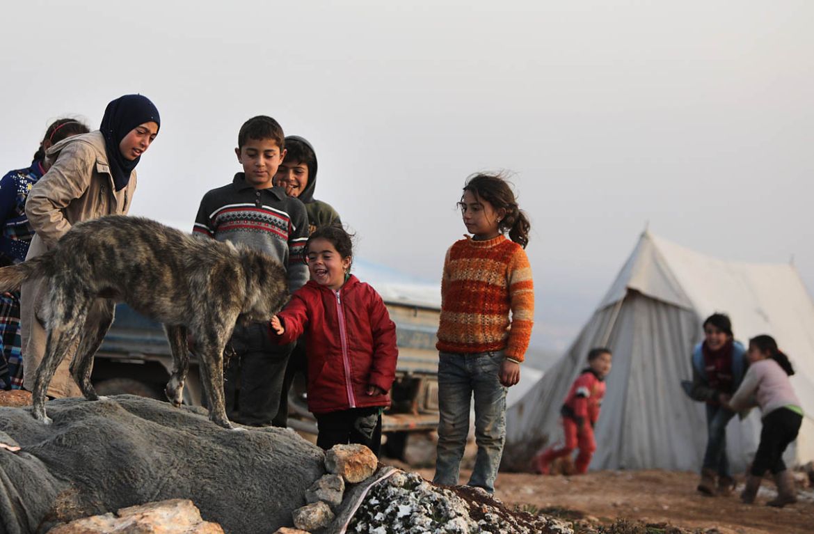 Syrian children play with a dog at a makeshift camp for displaced people who fled pro-regime forces attacks in the Idlib and Aleppo provinces, on February 18, 2020 north of the city of Idlib, near the