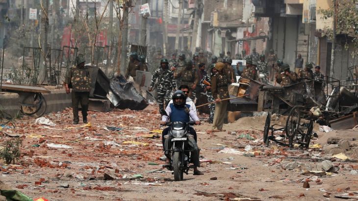 Men ride a motorcycle past security forces patrolling a street in a riot affected area after clashes erupted between people demonstrating for and against a new citizenship law in New Delhi, India, Feb