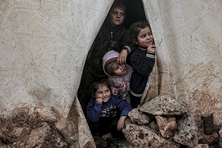 IDLIB, SYRIA - FEBRUARY 14: Children of Syrian families, who have been forcibly displaced due to the ongoing attacks carried out by Assad regime and its allies, look out of a tent''s zipper door at a c