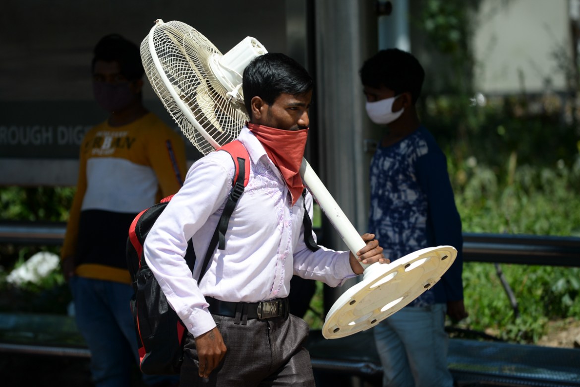 A migrant worker carrying a fan walks along a road as his leaves India''s capital for his home during a government-imposed nationwide lockdown as a preventive measure against the COVID-19 coronavirus,