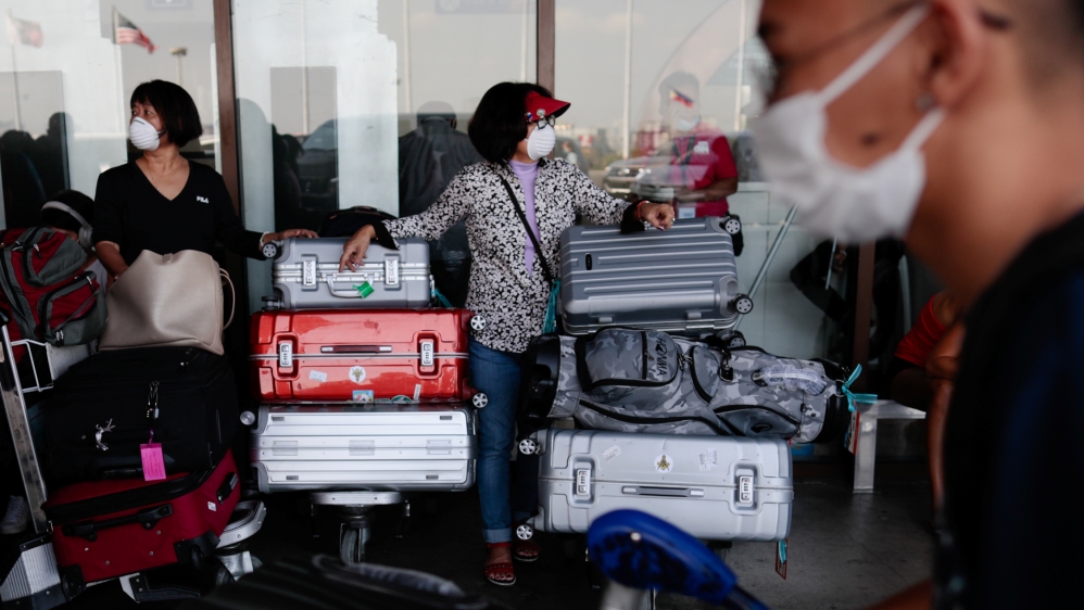 Passengers wearing masks stand by with their luggage outside the Ninoy Aquino International Airport in Paranaque, Metro Manila