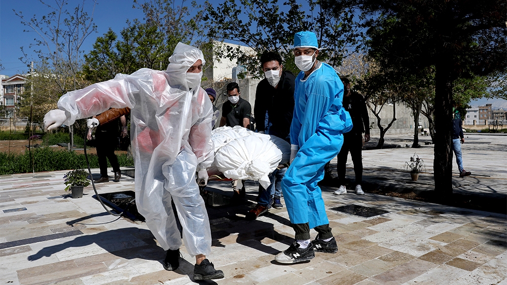 People wearing protective clothing carry the body of a victim who died after being infected with the new coronavirus at a cemetery just outside Tehran, Iran, Monday, March 30, 2020. The new coronaviru