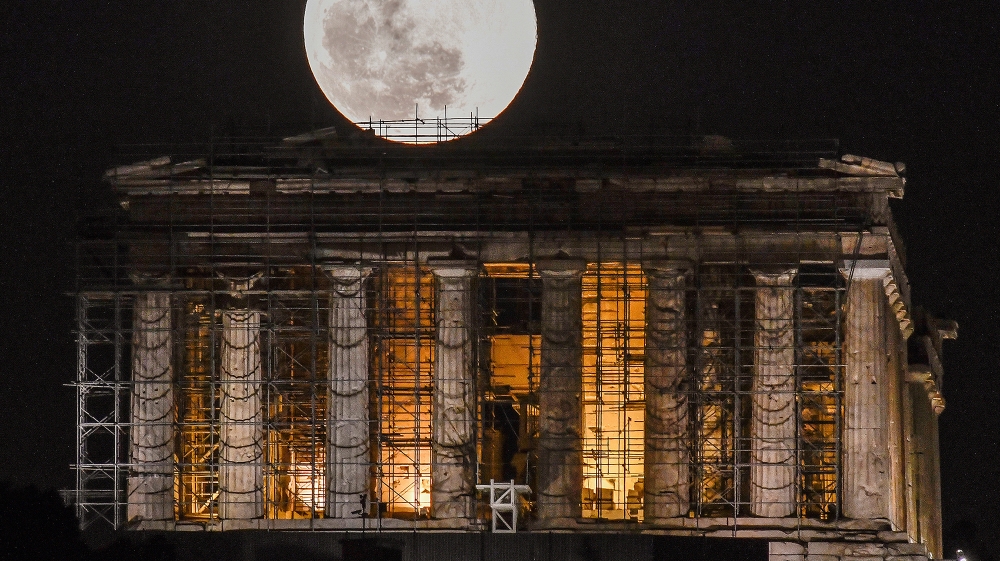 A full moon rises above Greek Parthenon Temple (438 BC), covered by scaffolding, at the Acropolis archaeological site in Athens on February 9, 2020 .  LOUISA GOULIAMAKI / AFP