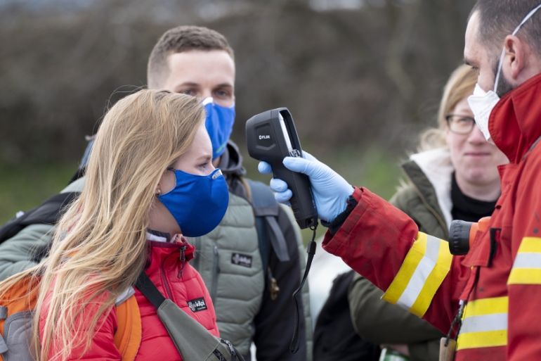 A Slovak firefighter checks the temperature of a woman wearing a protective facemask due to the coronavirus COVID-19 crossing the Bratislava-Jarovce border crossing between Austria and Slovakia on Mar