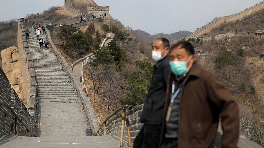 Men wearing protective masks stand as people hike along a section of the Great Wall in Badaling in Beijing, on its first day of re-opening after the scenic site's coronavirus related closure, China, M