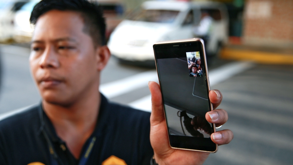 The gunman who has hostaged at least a dozen people shows a grenade on a video call with a policeman, witnessed by members of the media outside a mall in San Juan City, Metro Manila