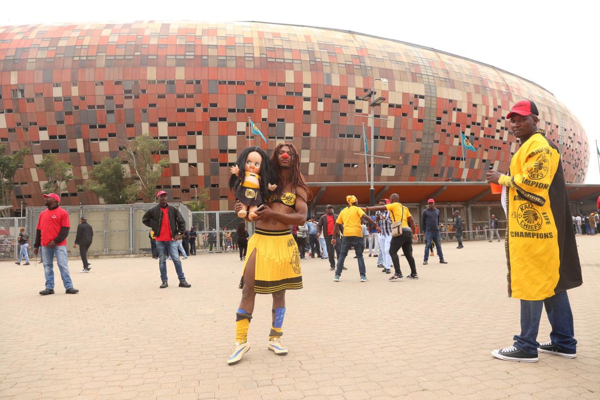 Holding a. doll is a Salmon a Kaizer chiefs fan at FNB stadium. He believes the doll represents love and peace , the clubs slogans. Cross dressing is big subculture especially amongst Orlando Pirates