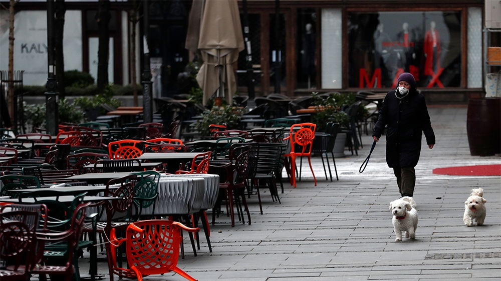 A woman walks with dogs in a deserted street amid the coronavirus outbreak in downtown Belgrade, Serbia, Thursday, March 26, 2020.   (AP Photo/Darko Vojinovic)