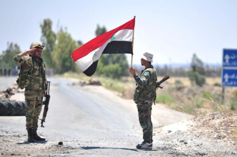 A member of forces loyal to Syria''s President Bashar al-Assad holds the national flag as another one gestures in al-Ghariya al-Gharbiya in Deraa province, Syria in this handout released on June 30, 20