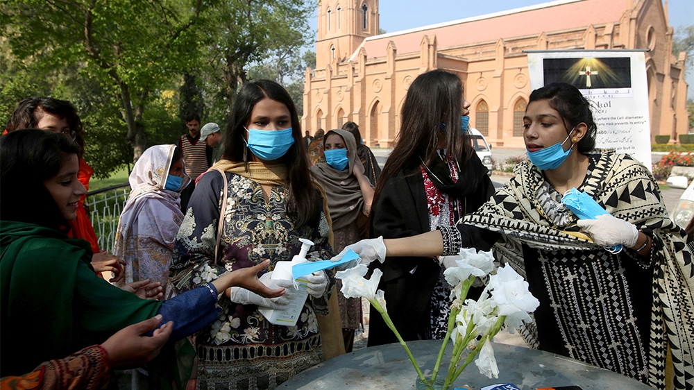 Christians volunteers distribute face mask among families arrive to attend Sunday mass at St. John’s Cathedral in Peshawar, Sunday, March 15, 2020. For most people, the new coronavirus causes only mil