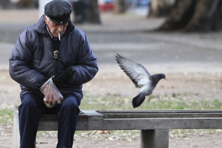 A retired man feeds pigeons at a public park in Buenos Aires