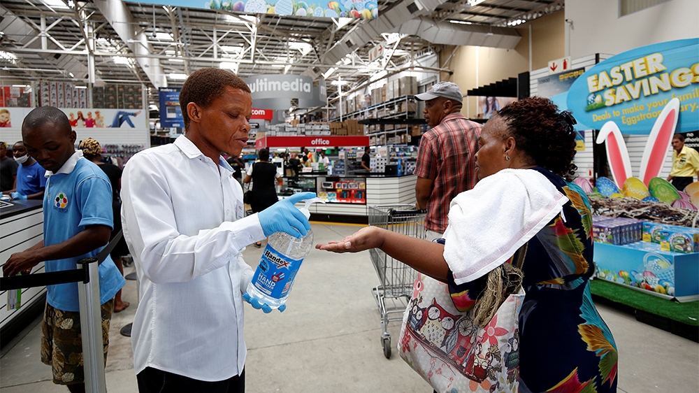 A store assistant gives people hand sanitiser as shoppers stock up on groceries at a Makro Store ahead of a nationwide 21 day lockdown in an attempt to contain the coronavirus disease (COVID-19) outbr