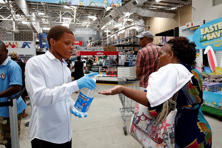 A store assistant gives people hand sanitiser as shoppers stock up on groceries at a Makro Store ahead of a nationwide 21 day lockdown in an attempt to contain the coronavirus disease (COVID-19) outbr