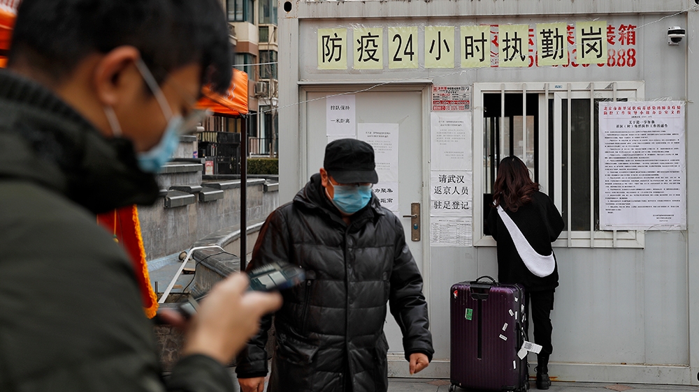 People pass a woman collecting her access card at a registration kiosk for people who returning from outside at a residential apartment building following the coronavirus outbreak in Beijing, Monday, 