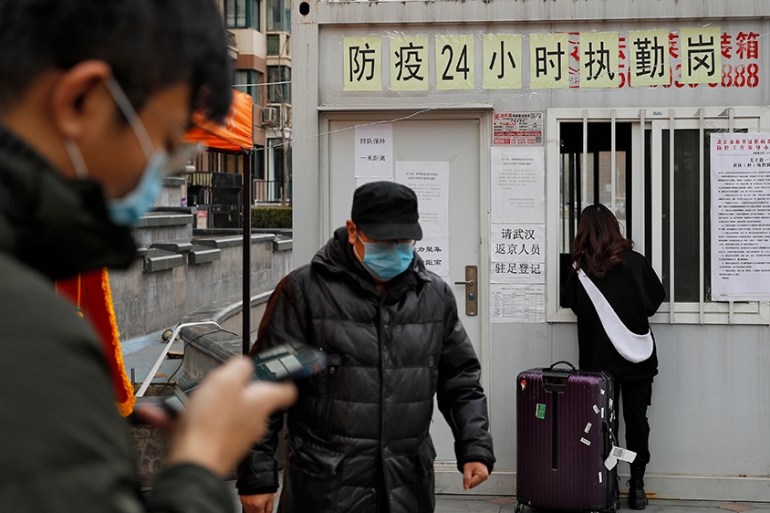 People pass a woman collecting her access card at a registration kiosk for people who returning from outside at a residential apartment building following the coronavirus outbreak in Beijing, Monday,