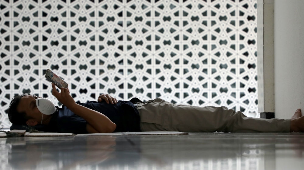 A Muslim wearing a protective mask uses his phone while lying down after the Friday prayers at National Mosque, following the coronavirus outbreak, in Kuala Lumpur, Malaysia, 