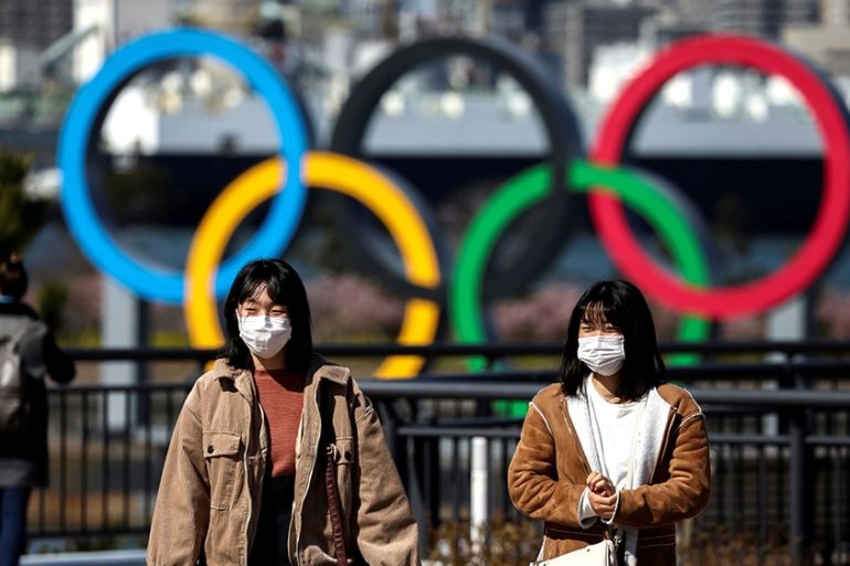 FILE PHOTO: People wearing protective face masks, following an outbreak of the coronavirus, are seen in front of the Giant Olympic rings at the waterfront area at Odaiba Marine Park in Tokyo, Japan, F
