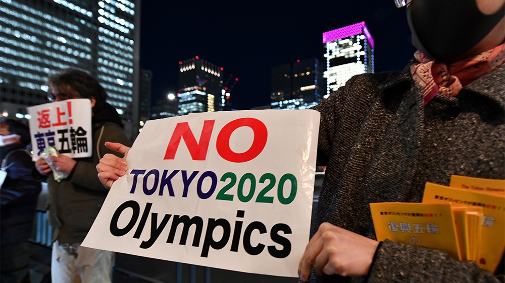 People opposed to the Tokyo 2020 Olympics display placards during a rally in front of Tokyo railway station on March 24, 2020. - The International Olympic Committee came under pressure to speed up its