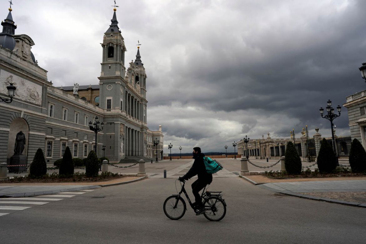 A delivery man cycles next to an empty square between La Almudena Cathedral and the Royal Palace during partial lockdown as part of a 15-day state of emergency to combat the coronavirus disease outbre