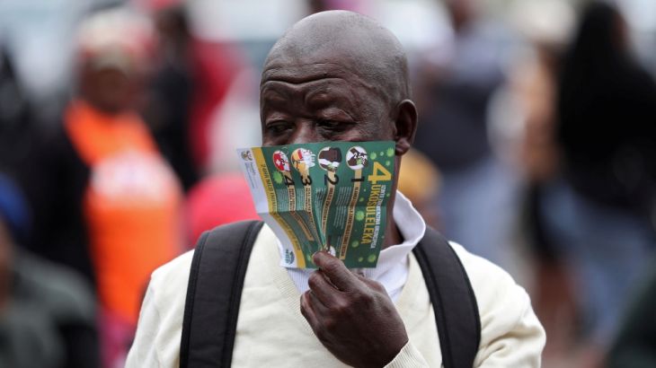 An elderly man covers his face with a pamphlet on coronavirus disease, while he queues for government grants despite coronavirus risks during a 21 day nationwide lockdown, aimed at limiting the spread