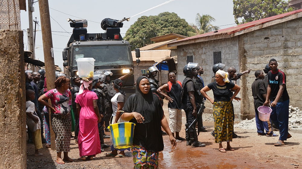 Residents and anti-riot police look on as a water cannon sprays water during demonstration in Conakry on March 21, 2020 on the eve of a constitutional referendum in the country. - Guinean President Al