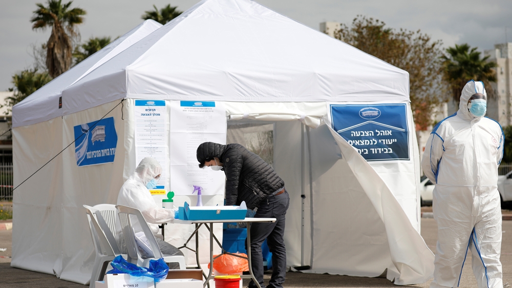 A paramedic in a protective suit helps a man as he prepares to vote in a special polling station set up by Israel's election committee so Israelis under home-quarantine, such as those