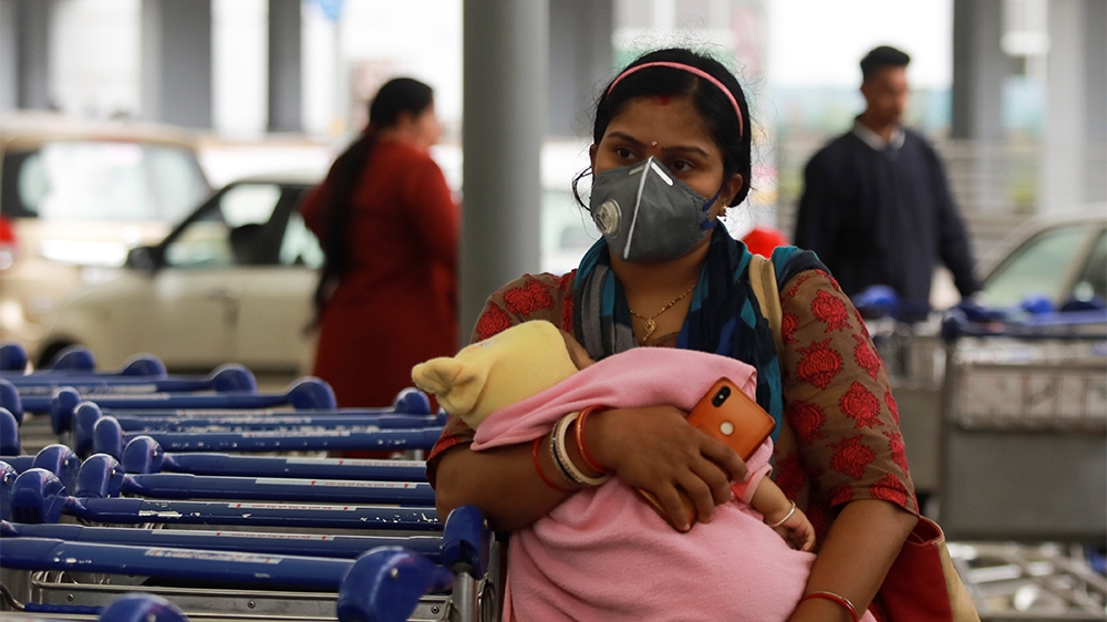 A passenger wearing a protective mask holds a baby as she waits outside an airport following an outbreak of the coronavirus disease (COVID-19), in New Delhi, India, March 14, 2020. REUTERS/Anushree Fa