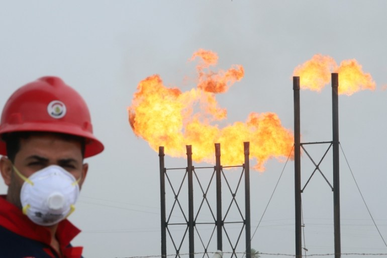 Flames emerge from flare stacks at Nahr Bin Umar oil field, as a worker wears a protective mask, following an outbreak of coronavirus, north of Basra