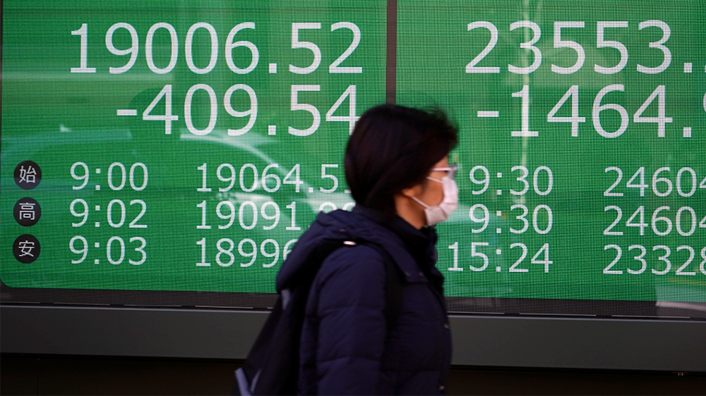 A woman walks past an electronic stock board showing Japan's Nikkei 225 and New York Dow index at a securities firm in Tokyo Thursday, March 12, 2020. (AP Photo/Eugene Hoshiko)
